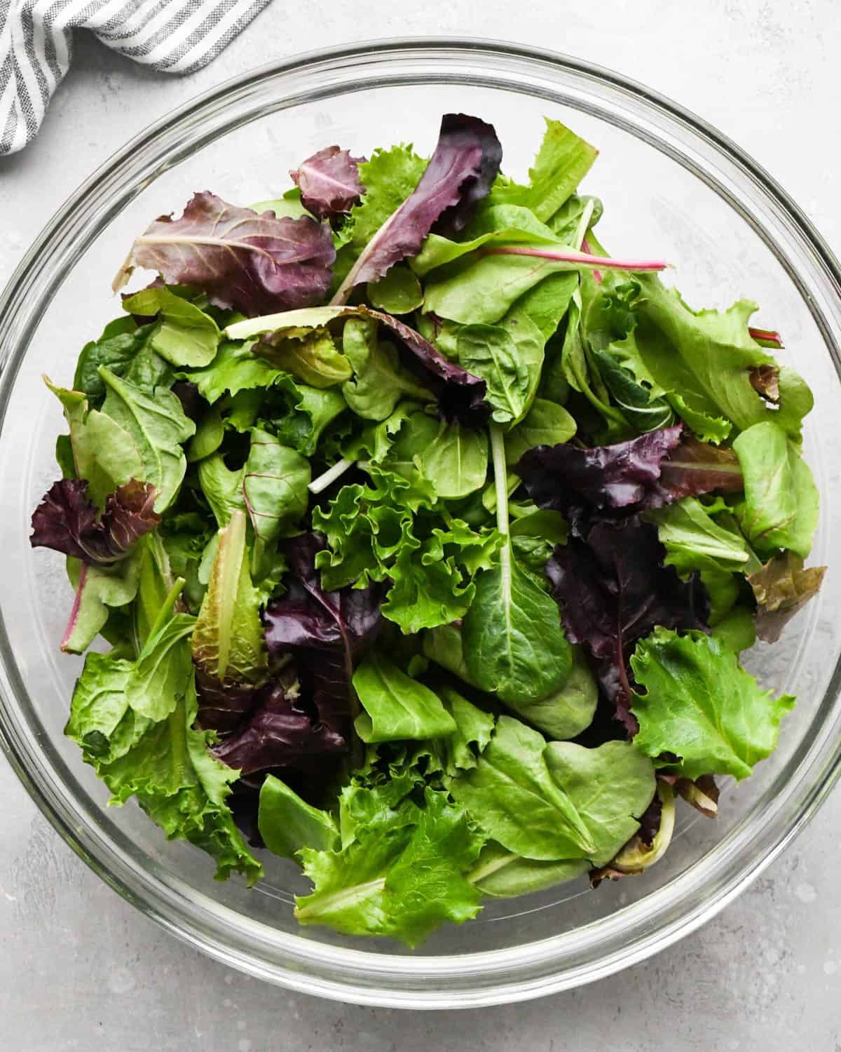 assembling a pear salad - spring mix in a glass serving bowl