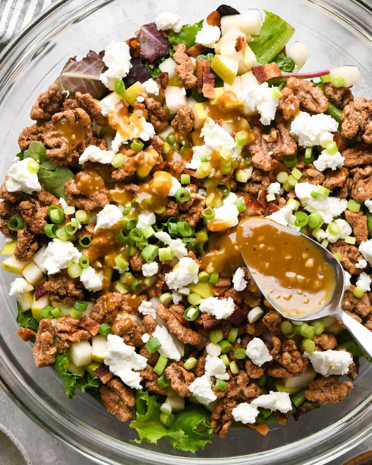 assembling a pear salad - dressing being drizzled over the ingredients in a glass bowl with a silver spoon