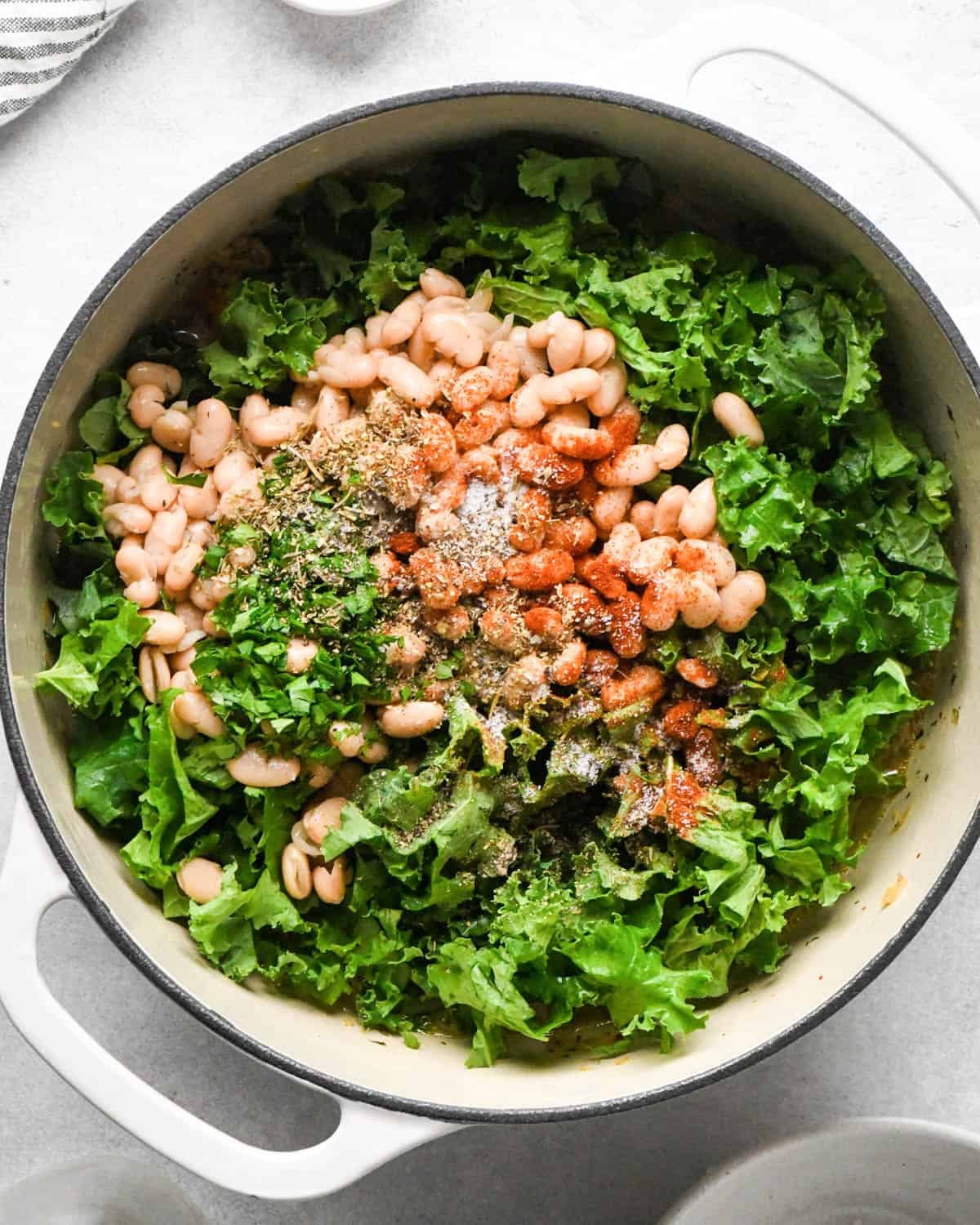 making sausage kale and white bean soup - kale, beans, spices and broth added to the pot