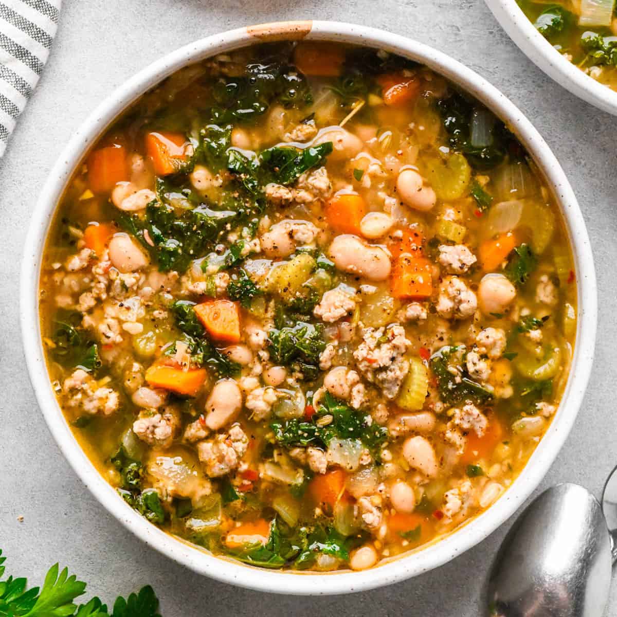 sausage, kale and white bean soup in a white ceramic bowl on a gray surface