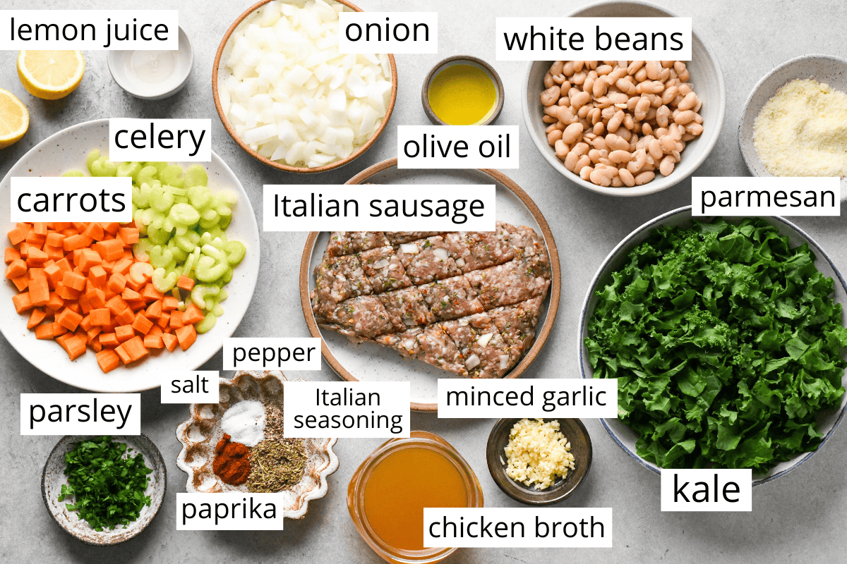 overhead photo of the ingredients for this sausage kale and white bean soup in bowls and labeled like Italian sausage, kale, carrots, celery, white beans, onion and more