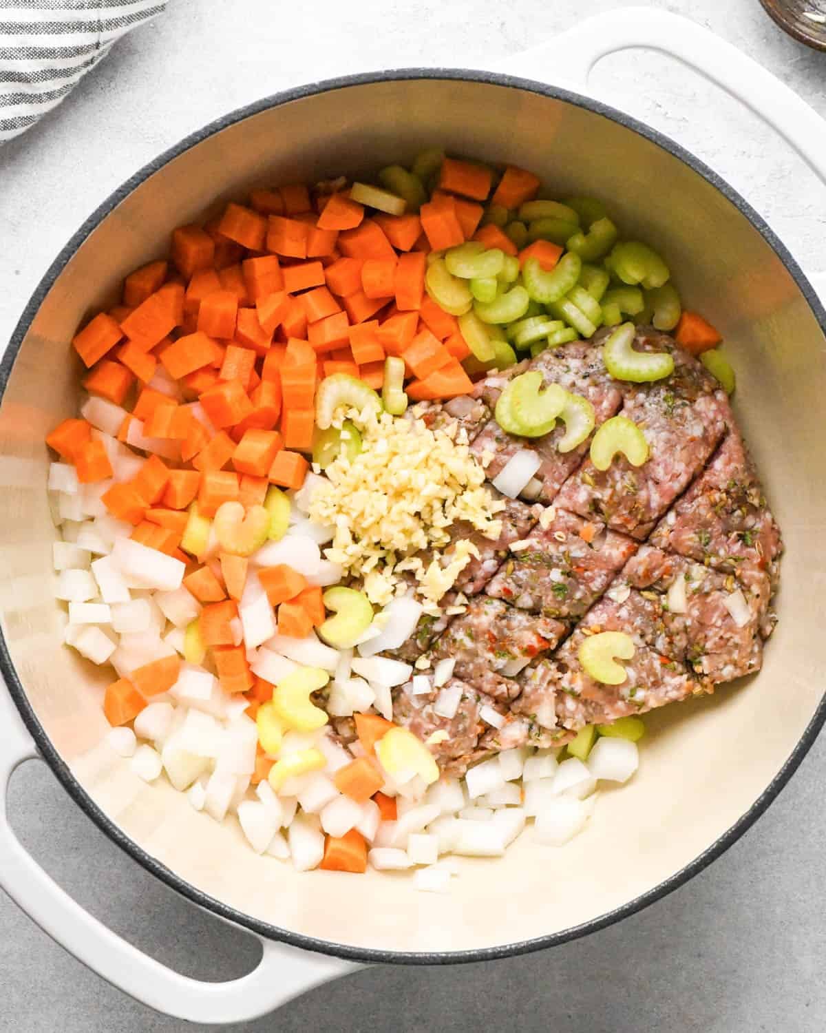 making sausage kale and white bean soup - italian sausage, carrots, celery, onion and garlic in a white pot with a black rim before cooking