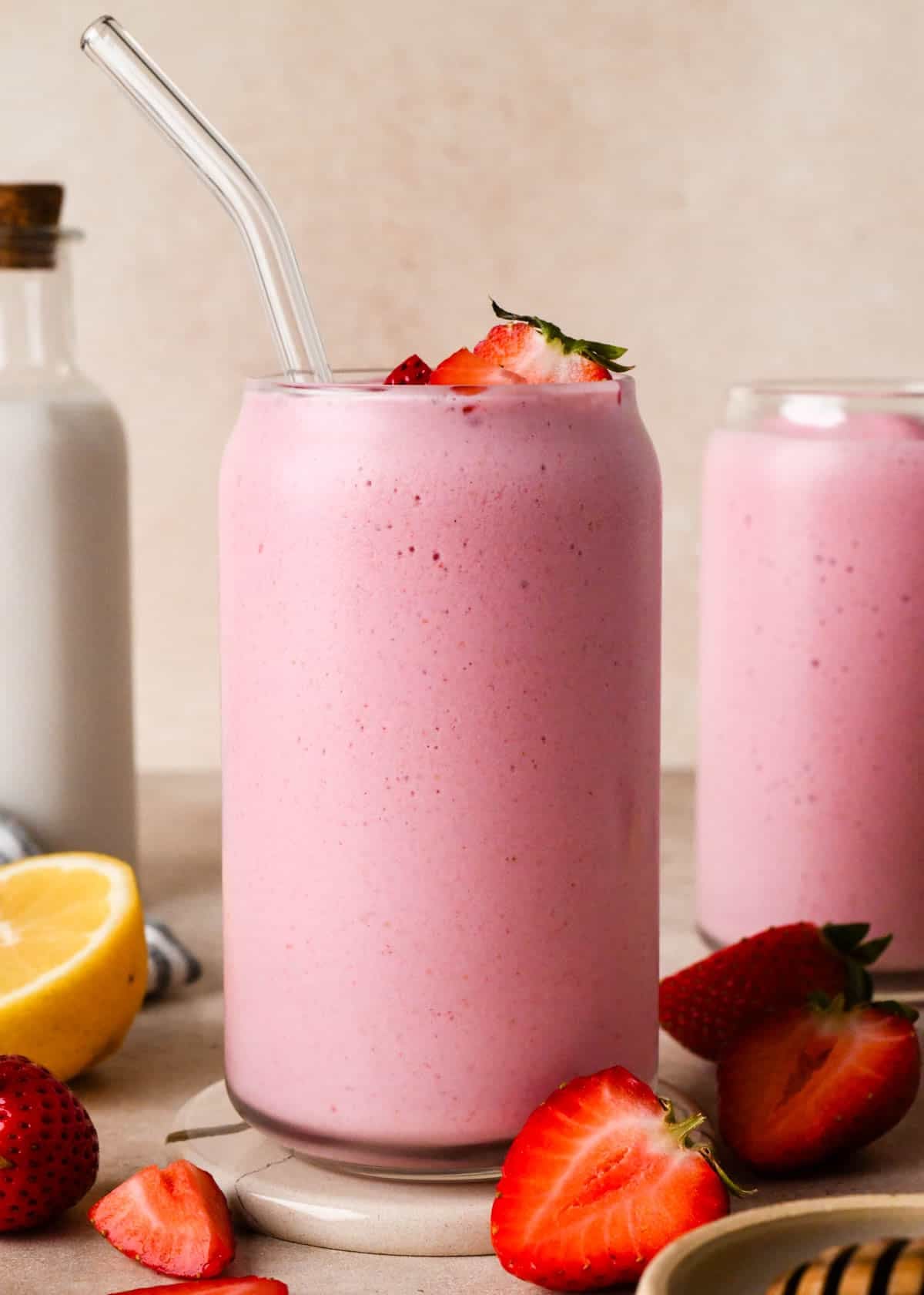 front view of 2 glasses of strawberry smoothie topped with chopped strawberries, surrounded strawberries and a lemon half