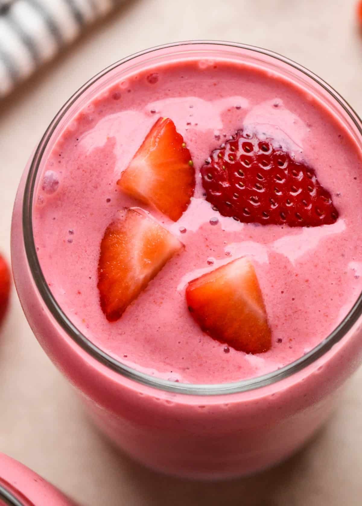 strawberry smoothie in a glass topped with chopped strawberries,