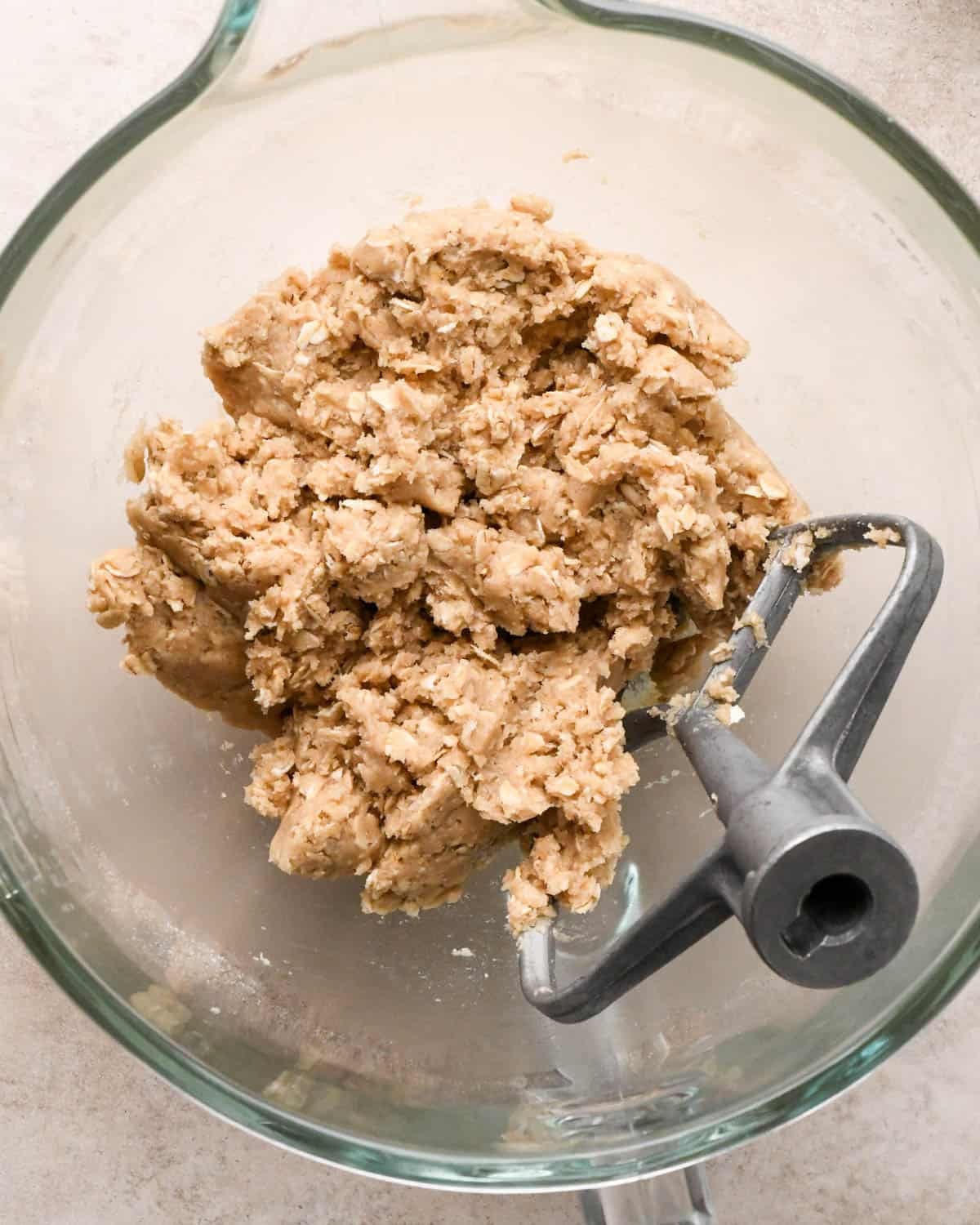 making vegan oatmeal cookies - dough in a glass mixing bowl with the paddle attachment after mixing in oats
