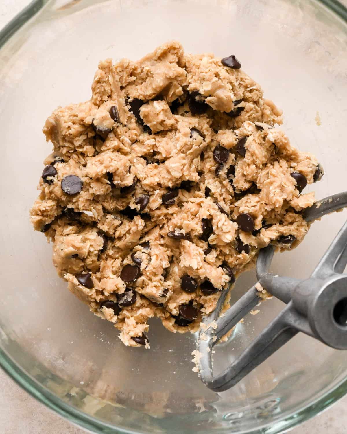 making vegan oatmeal cookies - dough in a glass mixing bowl with the paddle attachment after mixing in chocolate chips
