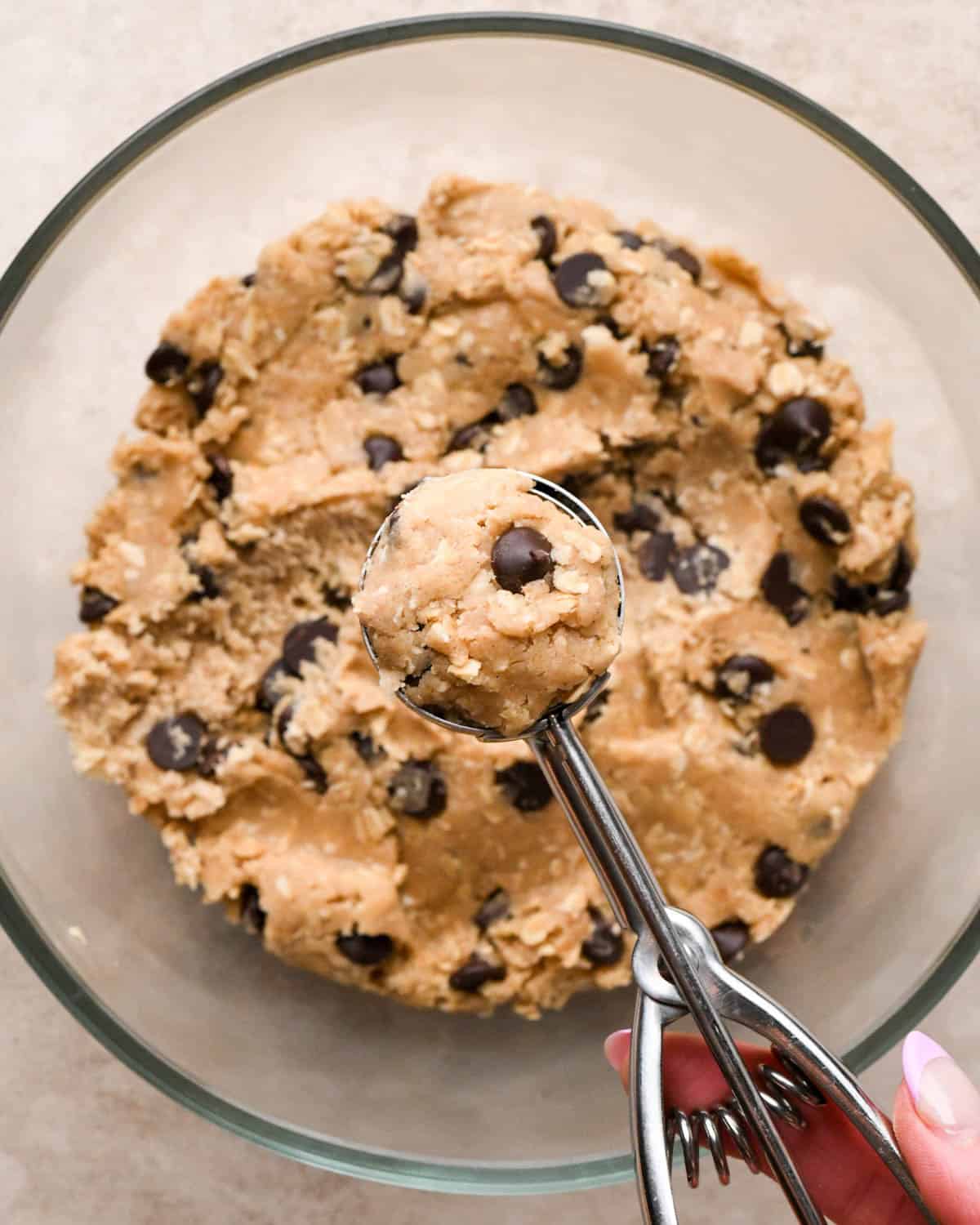 vegan oatmeal cookies dough in a glass bowl being scooped out with a metal cookie scoop