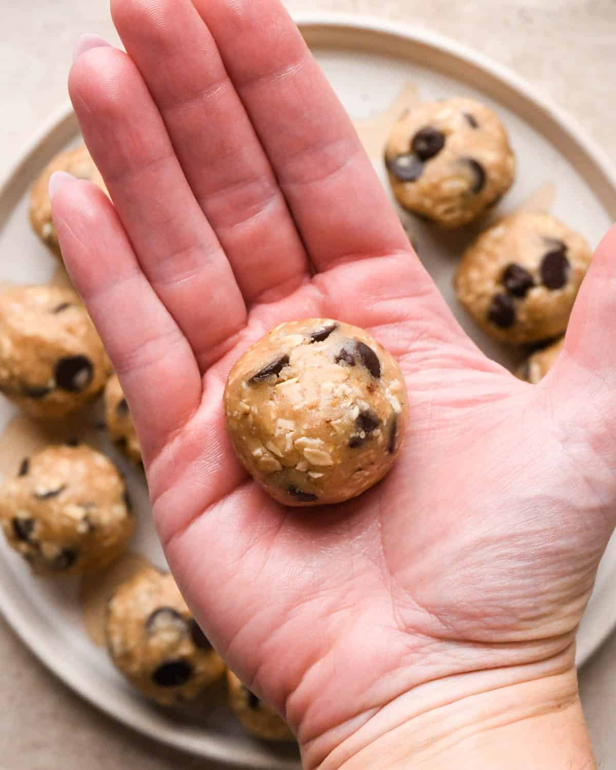 a hand holding vegan oatmeal cookie dough after it has been rolled into a ball, over a plate of dough balls