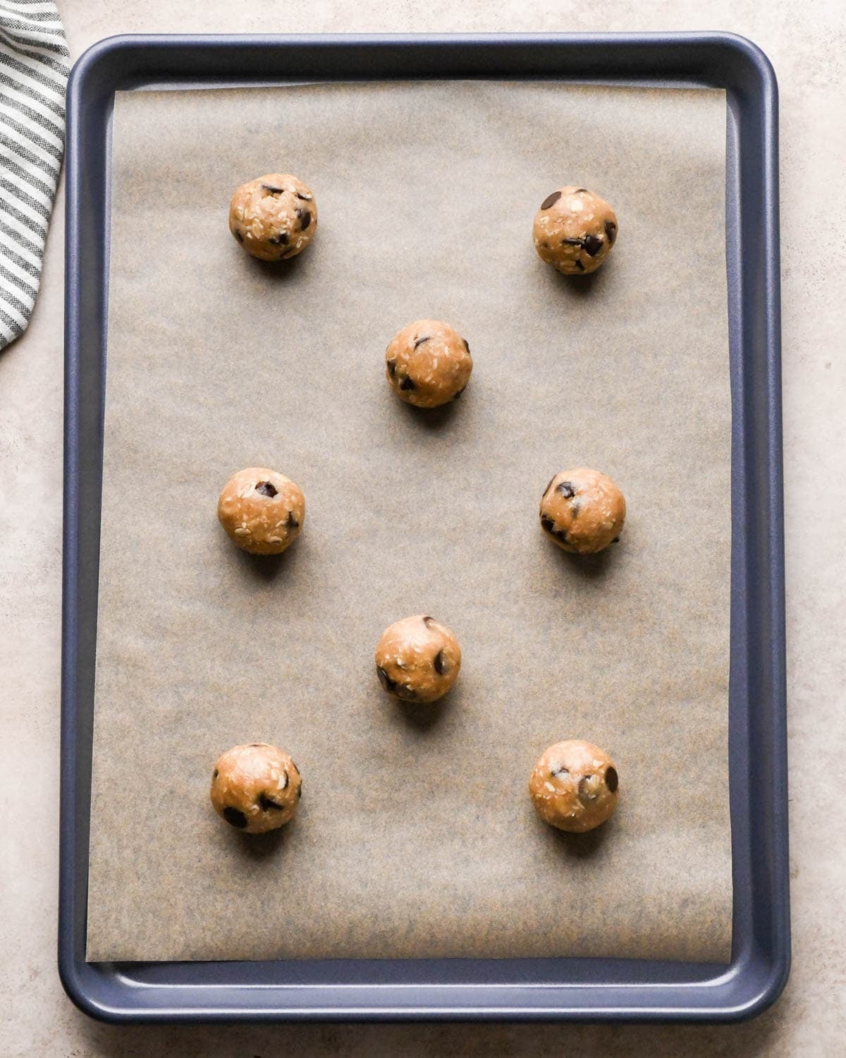 8 balls of vegan oatmeal cookie dough on a baking sheet lined with parchment paper before baking