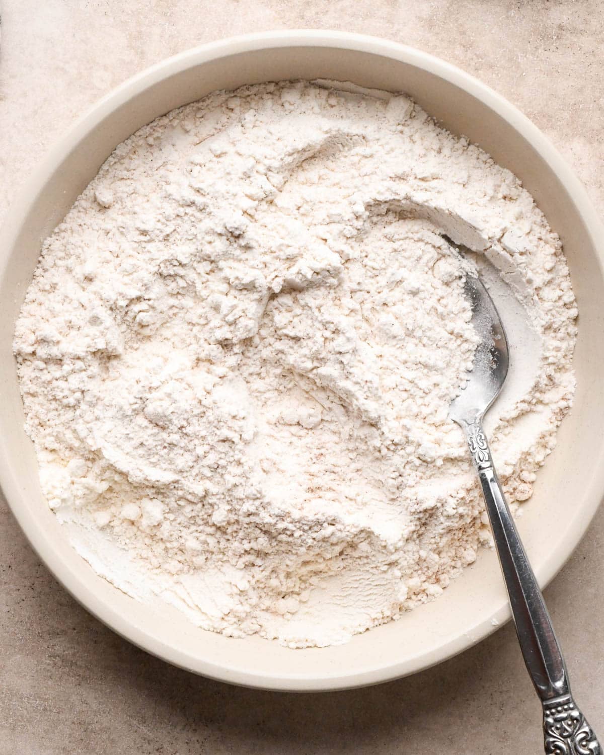 making vegan oatmeal cookies - dry ingredients in a white bowl mixed with a silver spoon