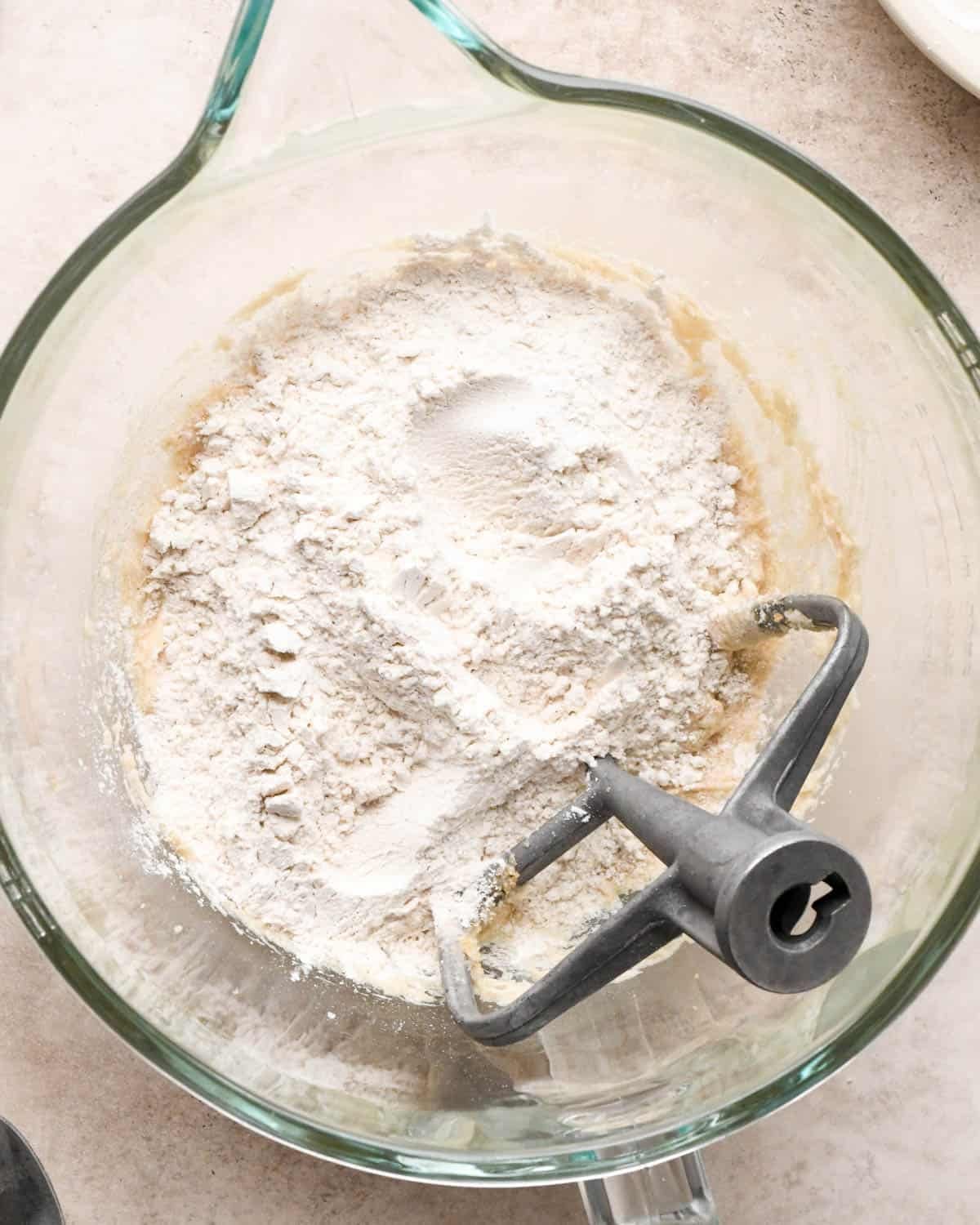 making vegan oatmeal cookies - flour added to the wet ingredients in a glass mixing bowl with the paddle attachment before mixing