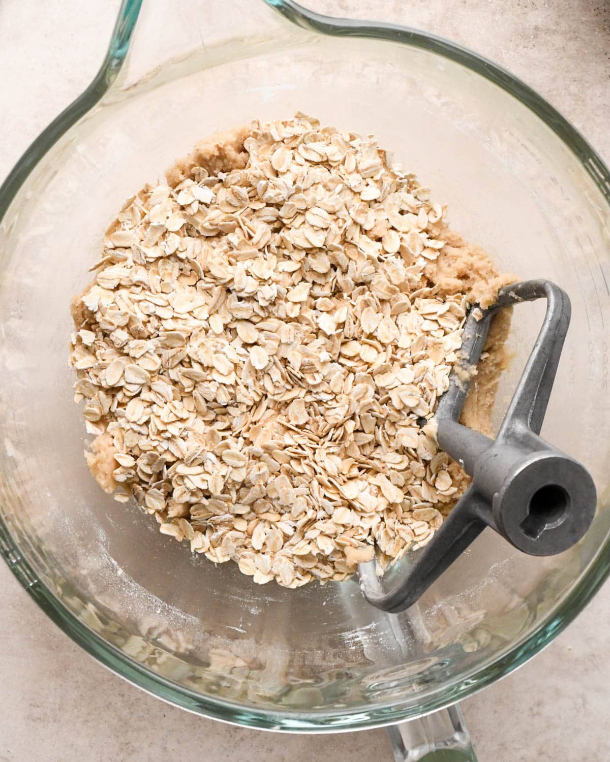 making vegan oatmeal cookies - adding oats to the dough in a glass mixing bowl with the paddle attachment, before mixing.
