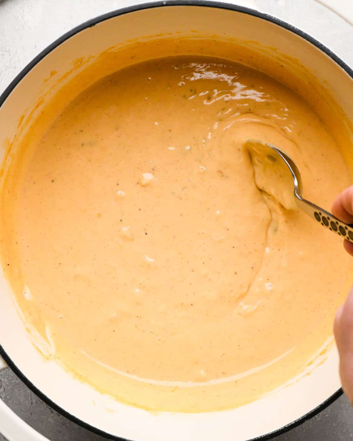 Making homemade queso: overhead photo of completed, thickened homemade queso in a large white pot being scooped up with a spoon.