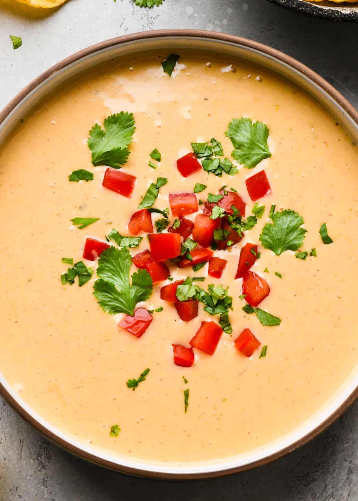 Bowl of homemade queso dip topped with diced red peppers and chopped cilantro.