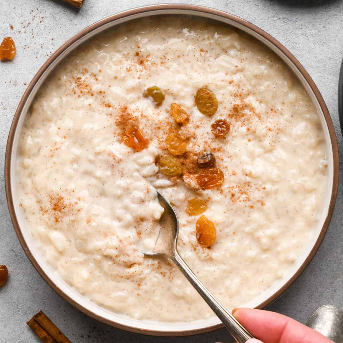 Overhead view of a bowl of creamy rice pudding topped with golden raisins and a dusting of cinnamon, with a spoon resting in the bowl.