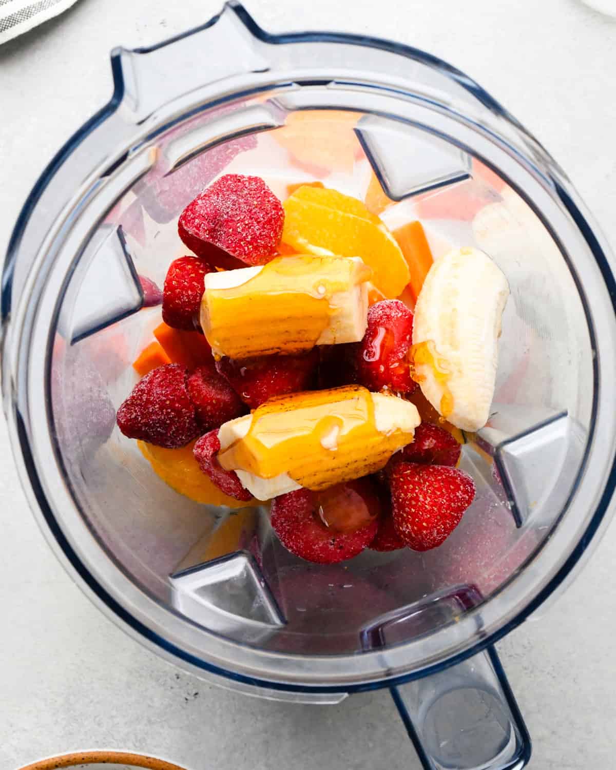 Making carrot fruit smoothie: overhead view of milk, oranges, strawberries, bananas, honey, and carrots sitting in a blender.