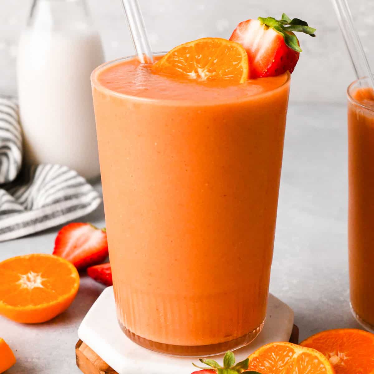 Grand verre de smoothie aux carottes et fruits, de couleur orange, garni d'une fraise et d'une tranche d'orange.