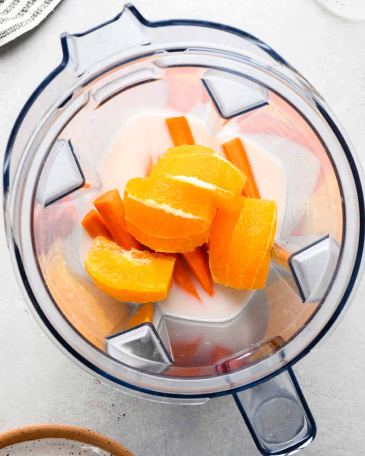 Making carrot fruit smoothie: overhead view of milk, oranges, and carrots sitting in a blender.