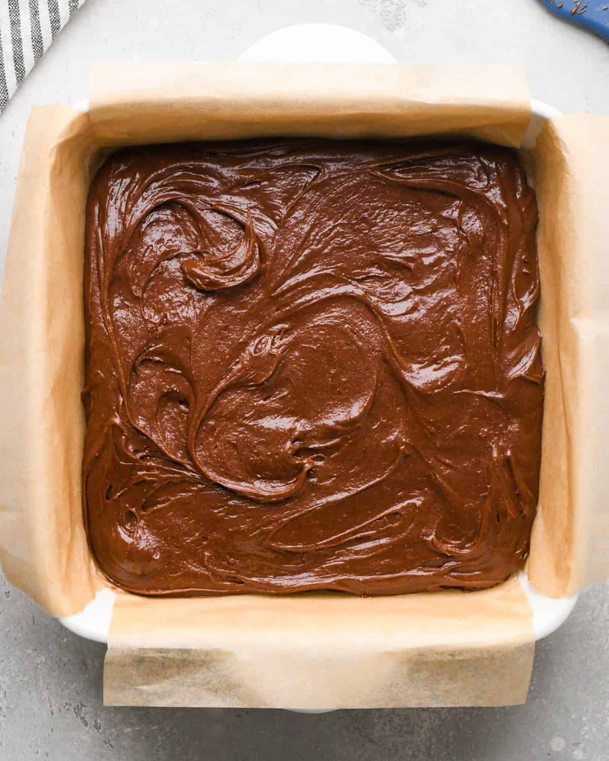 Making gluten-free brownies: overhead photo of brownie batter spread over parchment paper in a white square casserole dish.