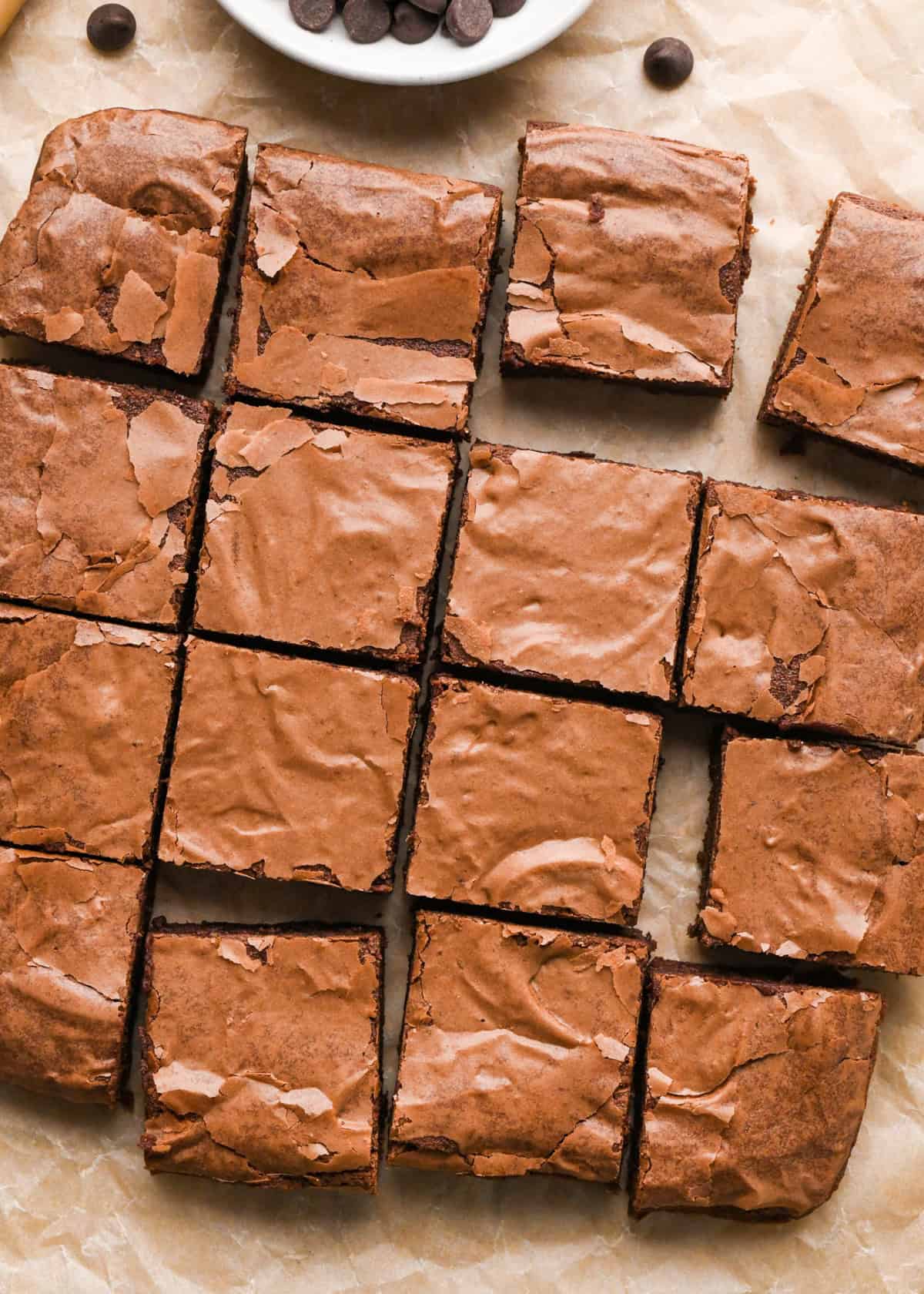Overhead photo of chocolate fudgy gluten-free brownies sitting on parchment paper and cut into squares for serving.