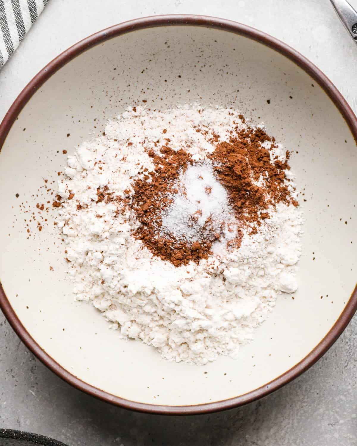 Making gluten-free brownies: overhead photo of dry ingredients added to a white speckled bowl.