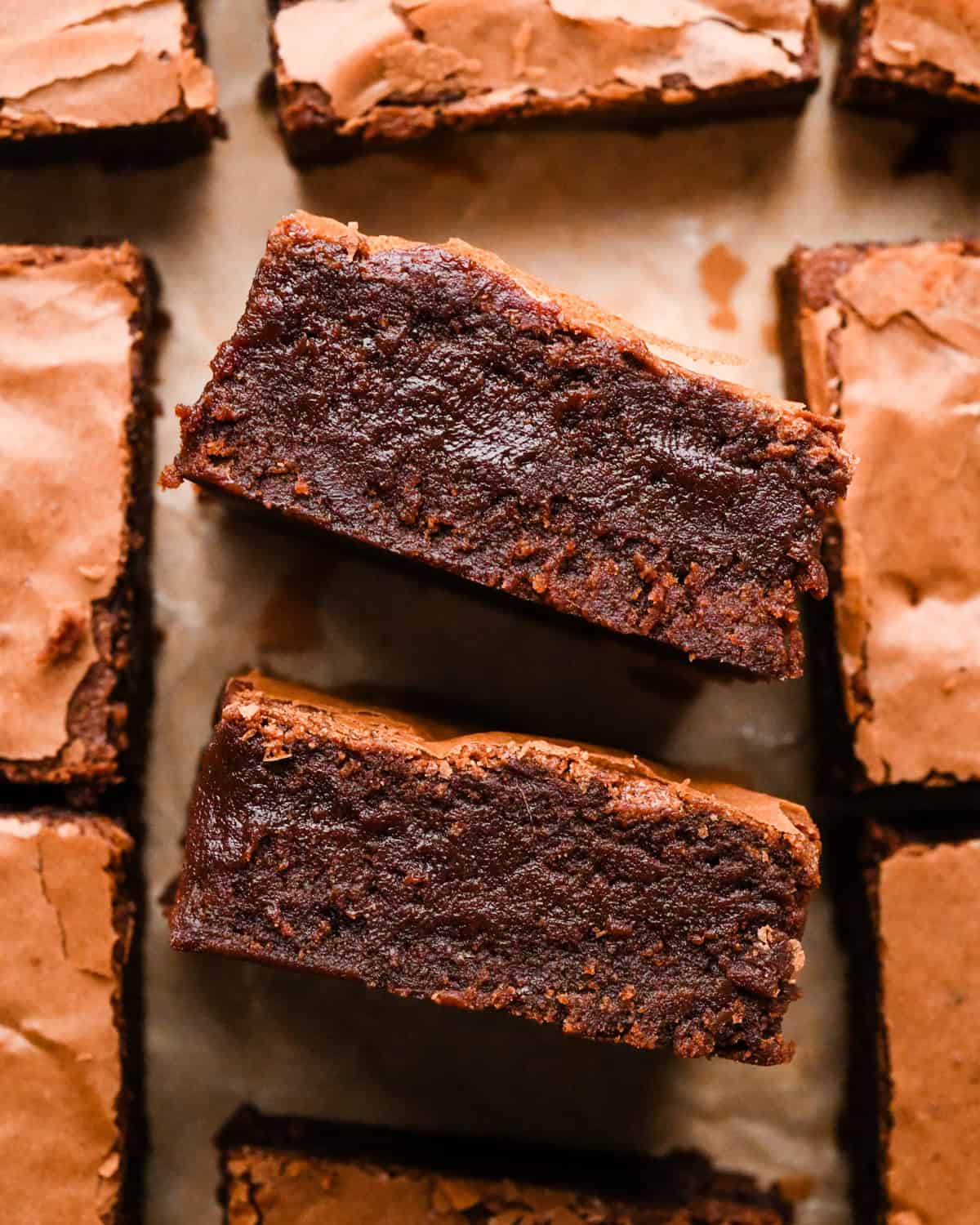 Overhead photo of rich, fudgy gluten-free brownies with a crackly top, shown close-up on parchment paper.