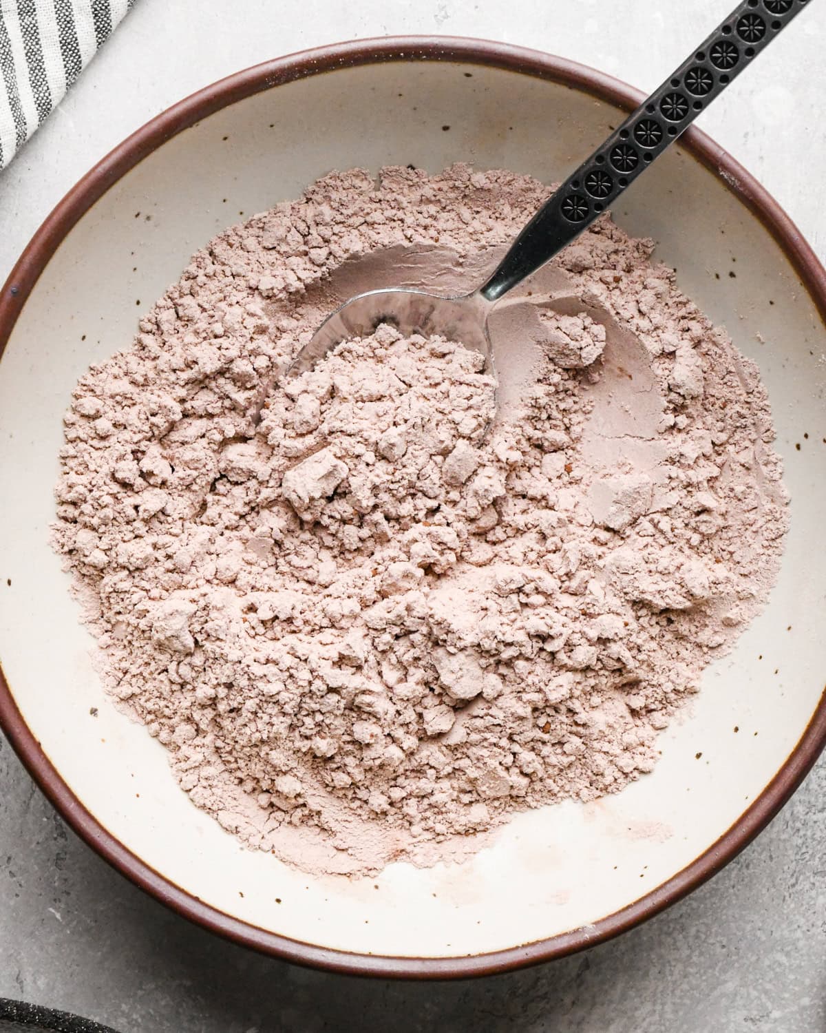 Making gluten-free brownies: overhead photo of dry ingredients added to a white speckled bowl and mixed together with a spoon.