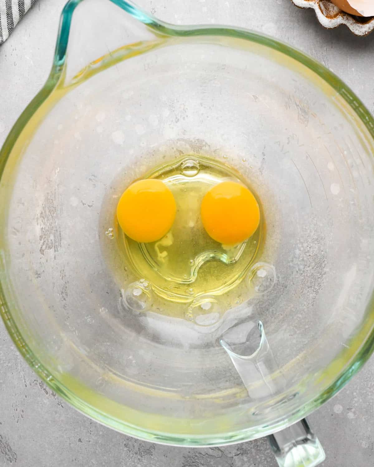 Making gluten-free brownies: overhead photo of 2 eggs cracked into a clear glass measuring bowl.