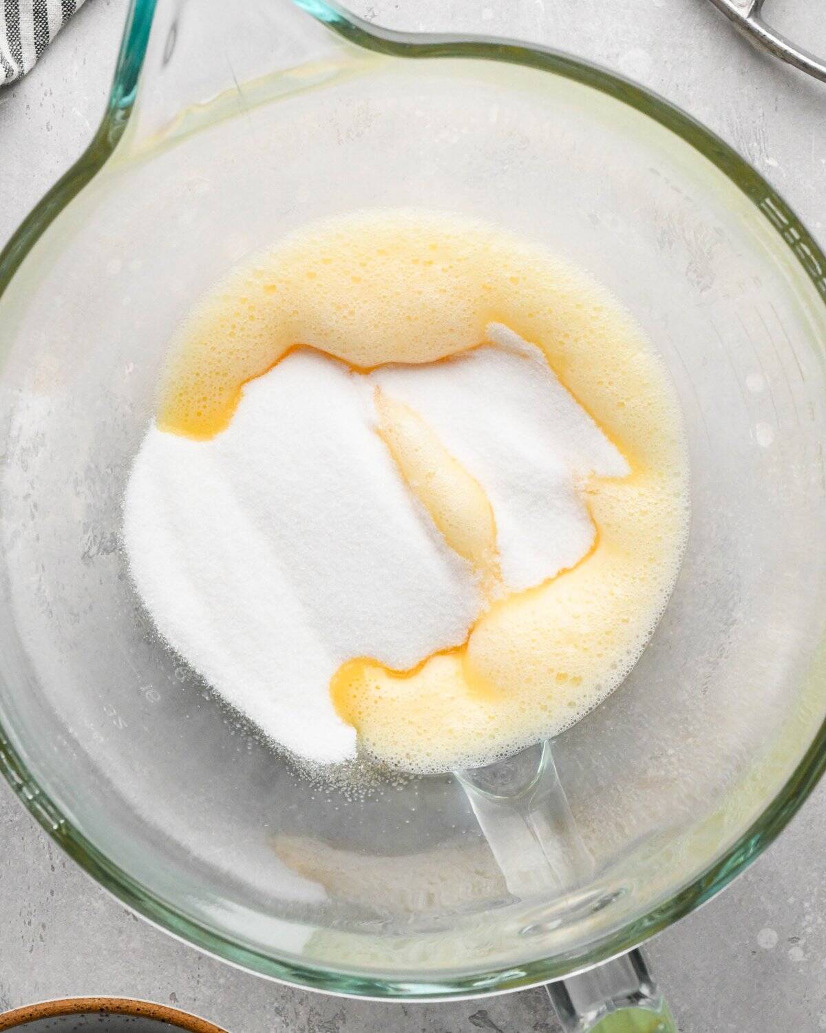 Making gluten-free brownies: overhead photo of sugar being added to beaten eggs in a clear glass measuring bowl.