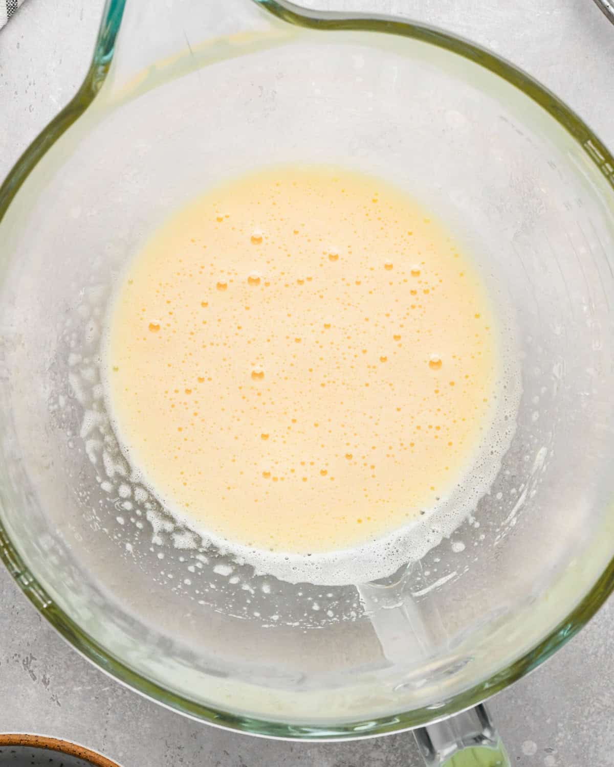 Making gluten-free brownies: overhead photo of sugar being added to beaten eggs in a clear glass measuring bowl and mixed together.