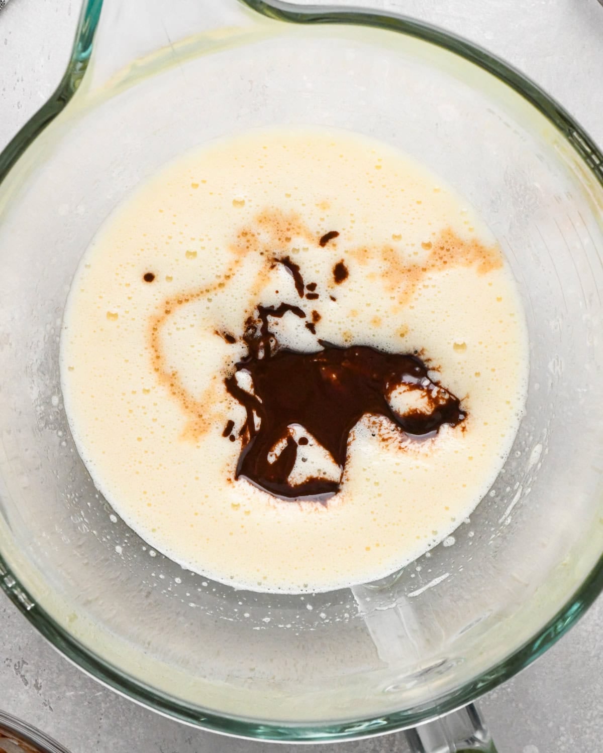 Making gluten-free brownies: overhead photo of melted chocolate mixture being added to egg and sugar mixture in clear glass measuring bowl.