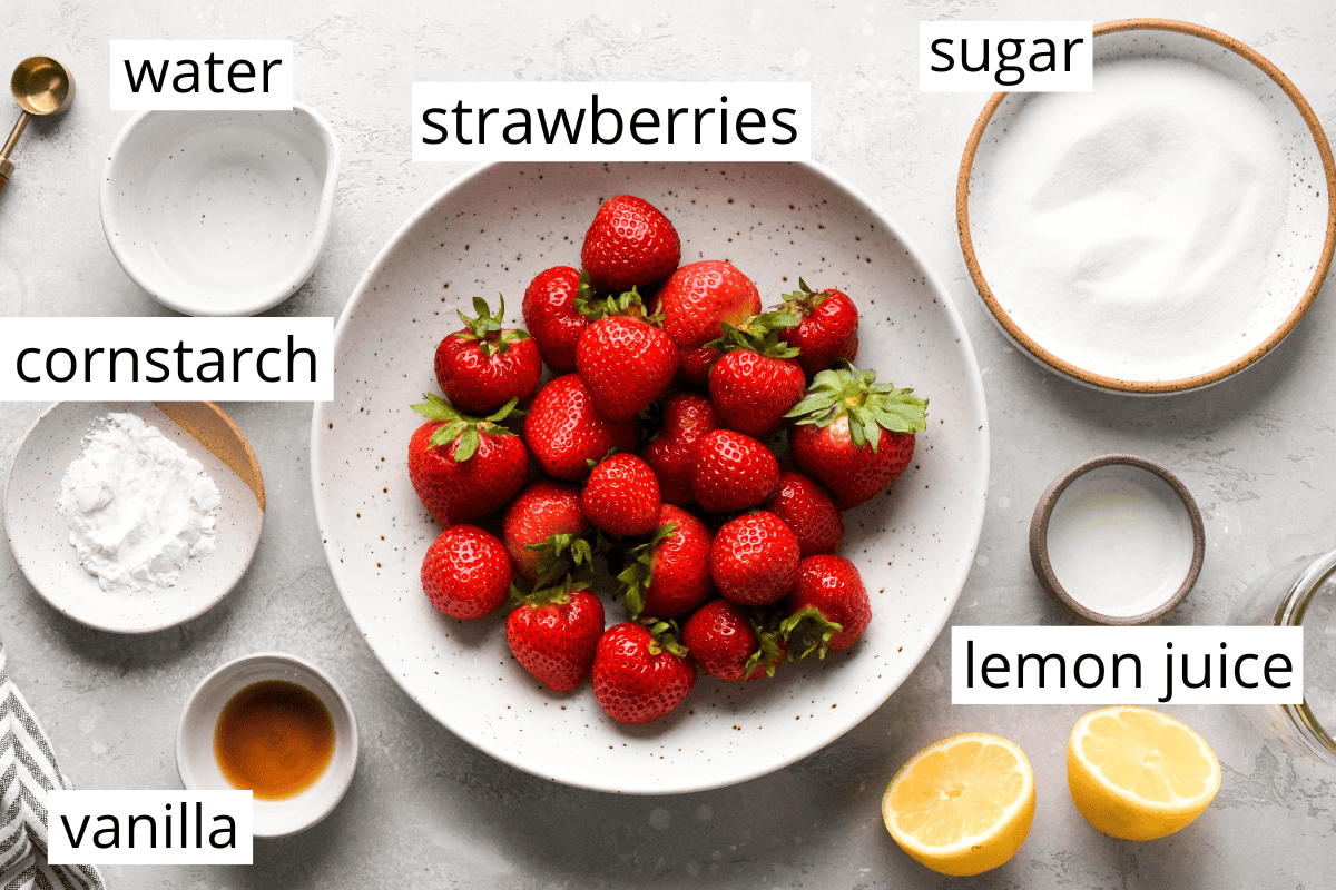 Overhead photo of the ingredients for homemade strawberry sauce, including fresh strawberries, cornstarch, vanilla, lemon juice, water, and sugar.