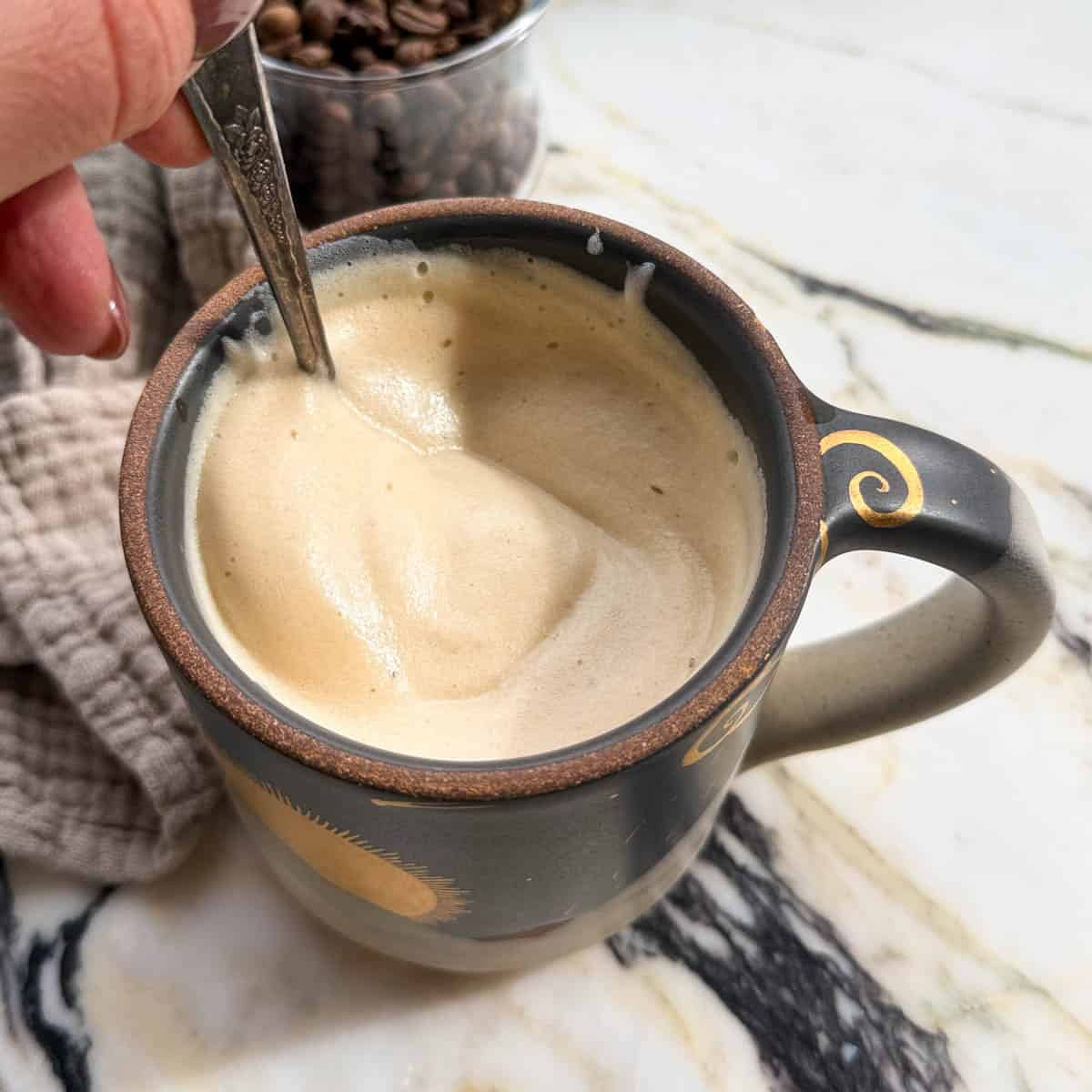 latte recipe being stirred in a navy, cream and gold mug with a silver spoon. 