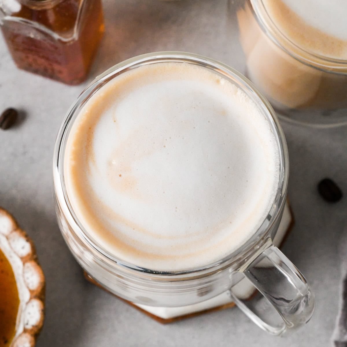 How to make a latte: overhead photo of a completed homemade latte topped with frothy milk and surrounded by coffee beans and honey on a light surface.