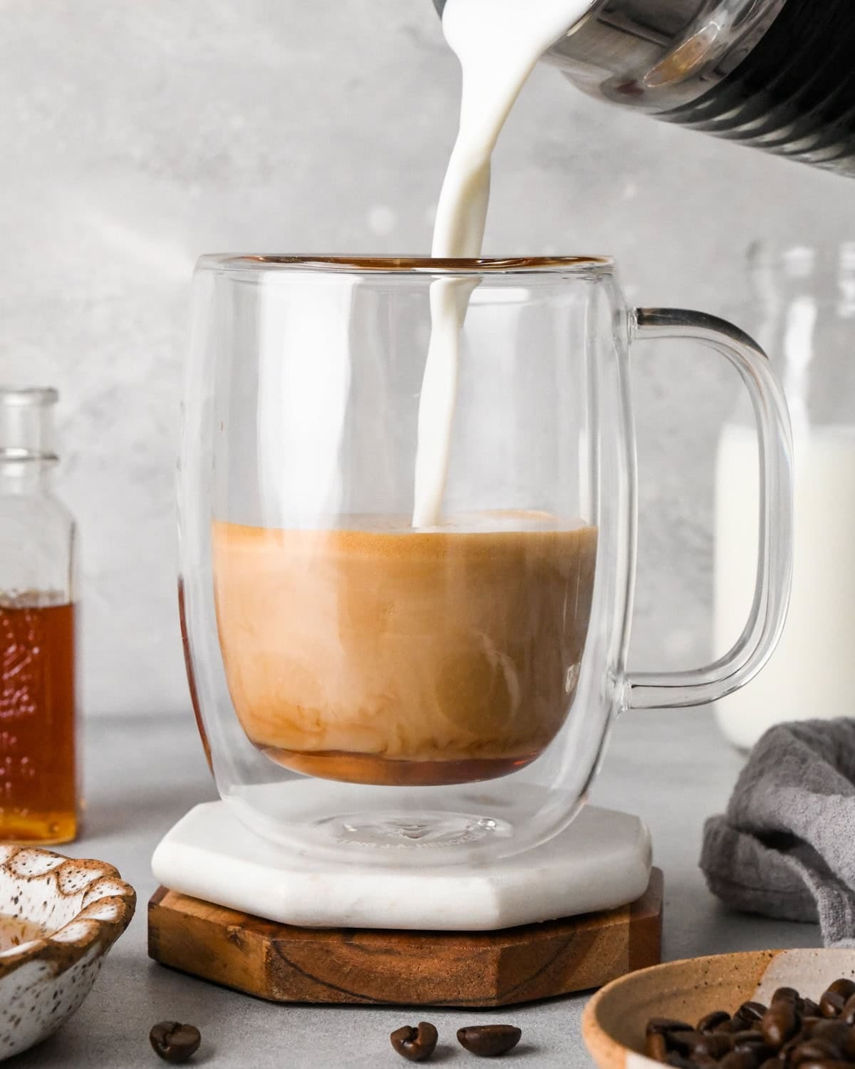How to make a latte: front-view photo of milk being added to espresso mixture in a clear coffee mug.