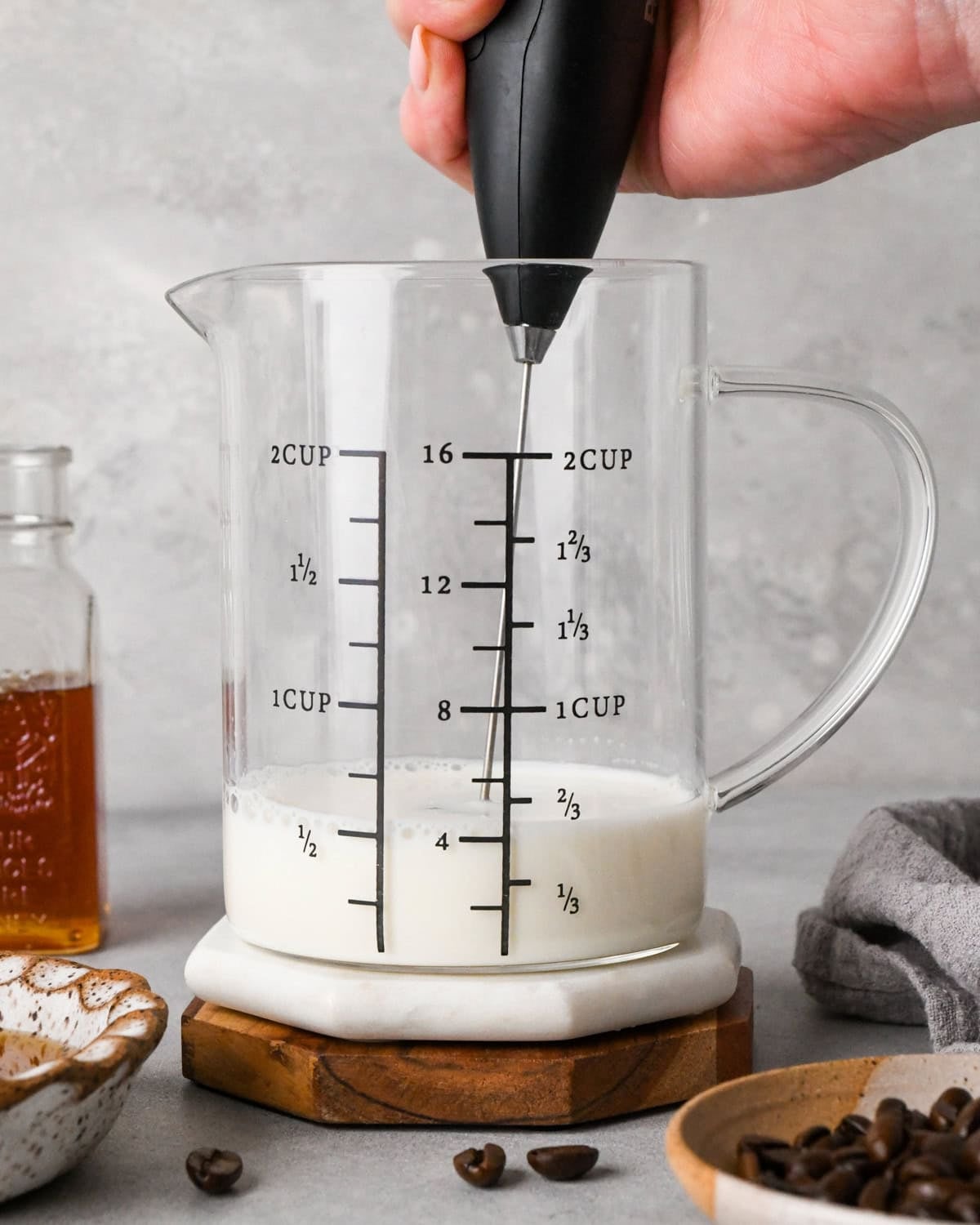 How to make a latte: front-view photo of a handheld frother frothing milk in a clear measuring cup.