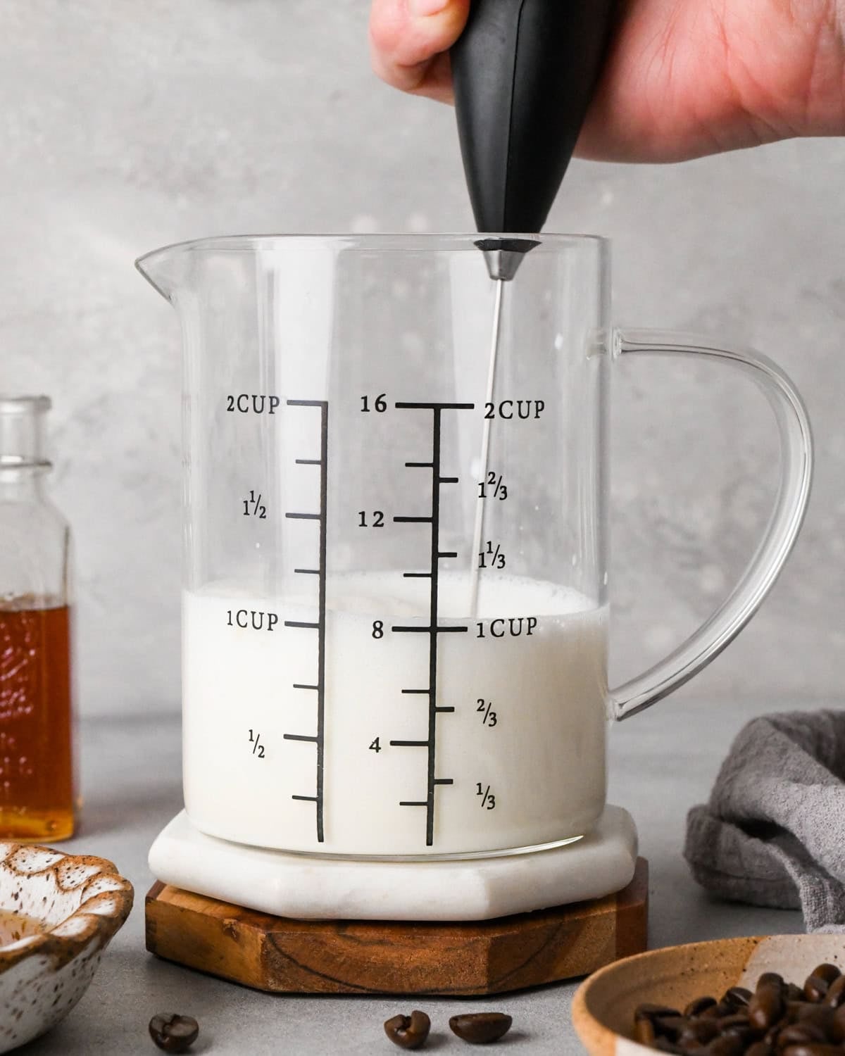 How to make a latte: front-view photo of a handheld frother frothing milk in a clear measuring cup.