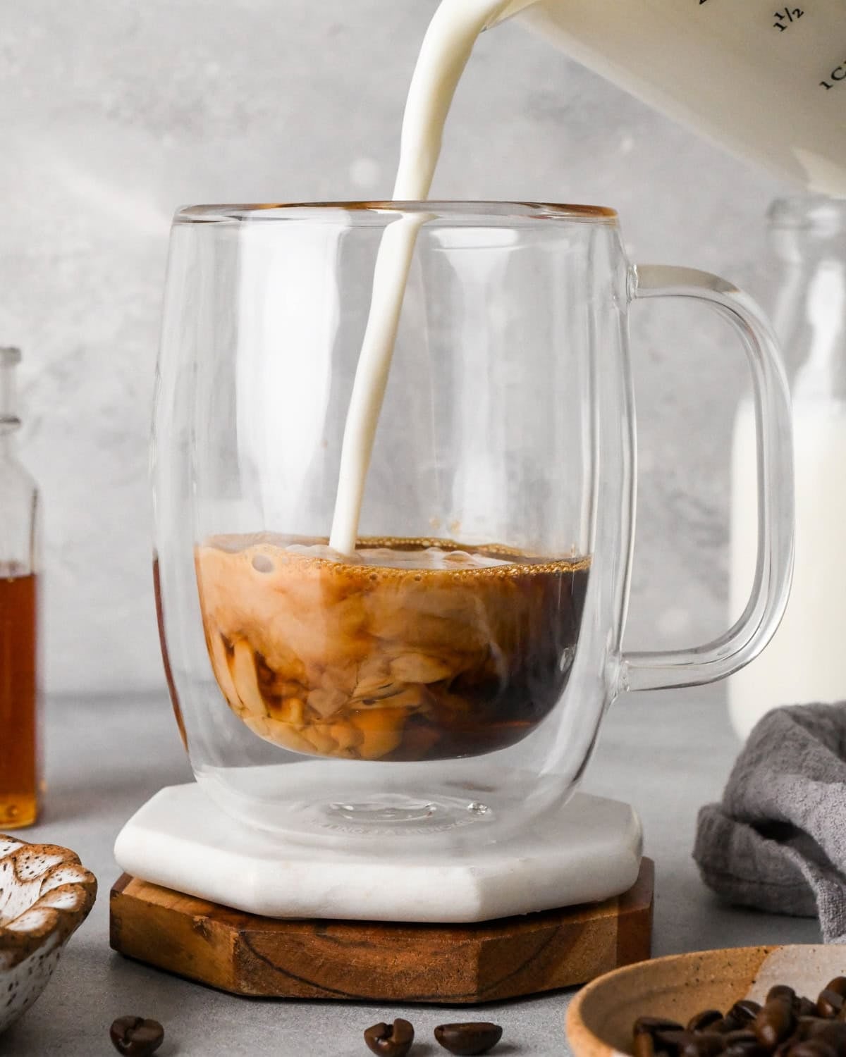 How to make a latte: front-view photo of a frothed milk being poured into espresso mixture in a clear coffee mug.
