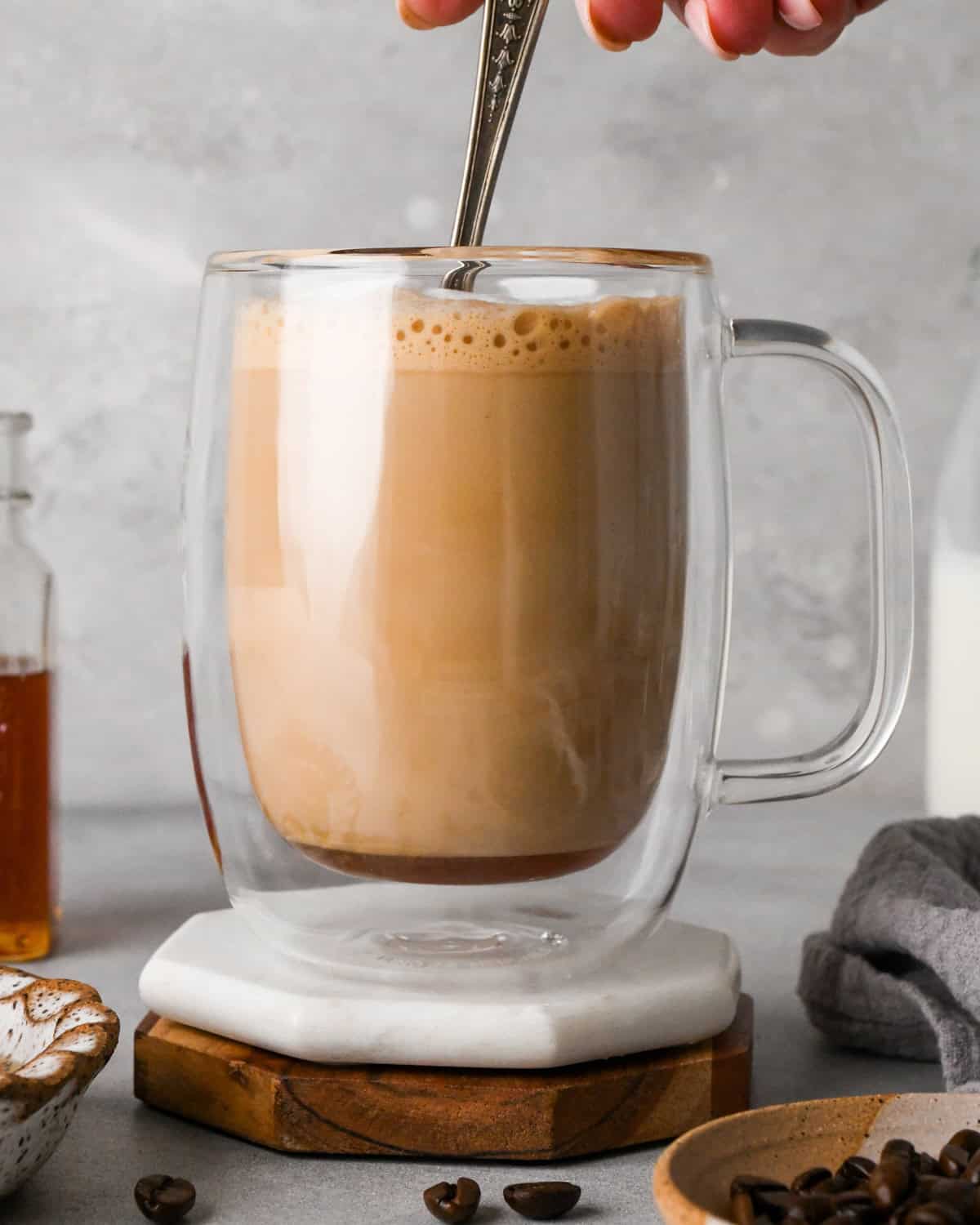 How to make a latte: front-view photo of espresso, honey, and frothed milk in a clear coffee mug being stirred with a spoon.