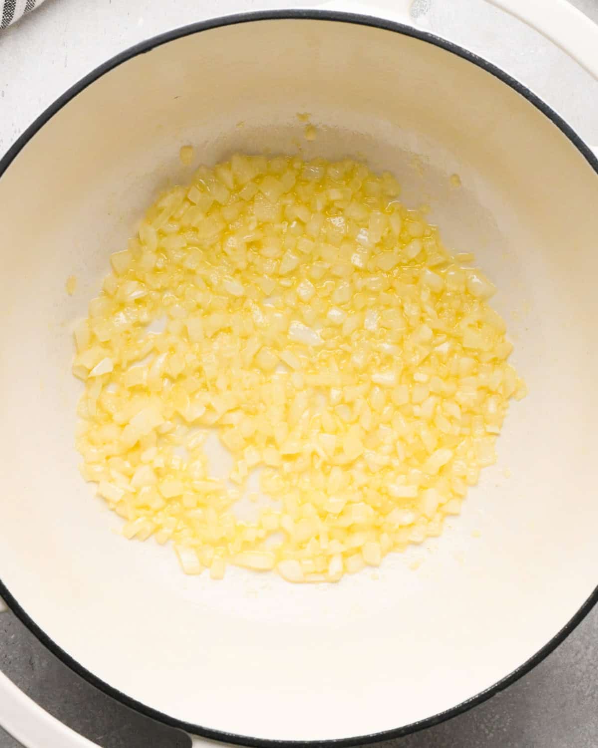 Making homemade queso: overhead photo of diced onion, minced garlic, and butter being sautéed together in a large white pot.