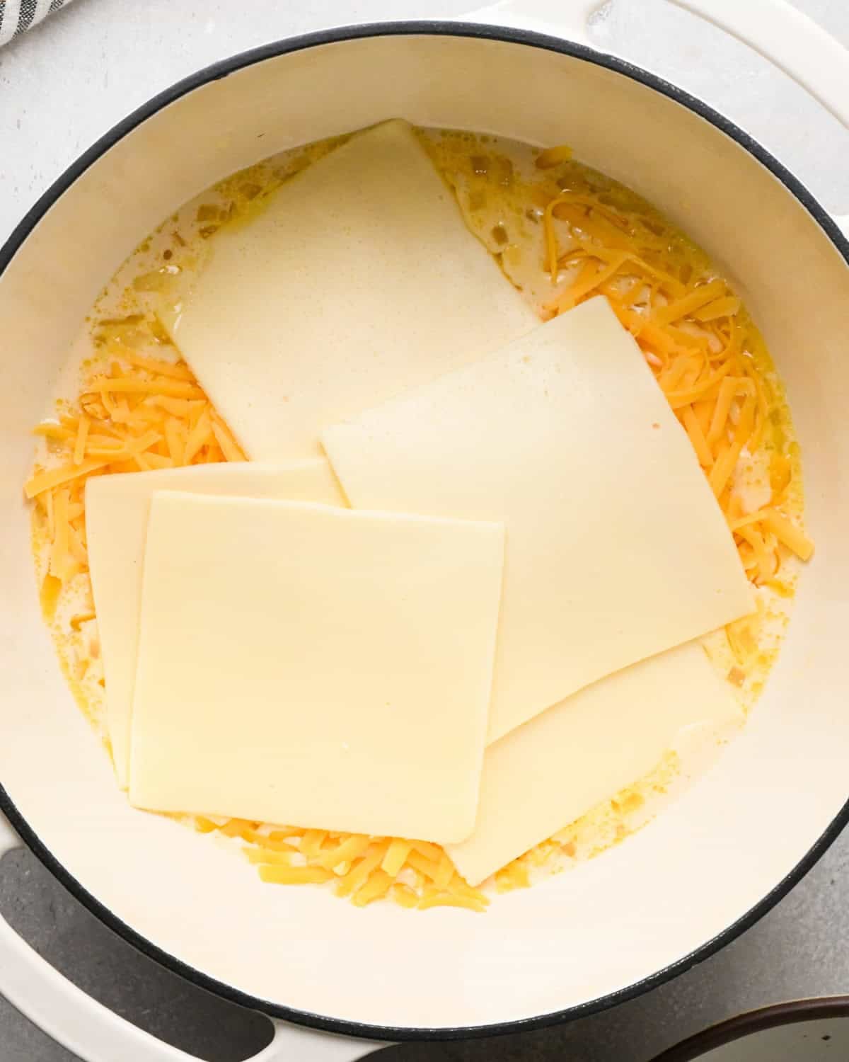 Making homemade queso: overhead photo of white American cheese being added to large white pot with the simmering sauce.