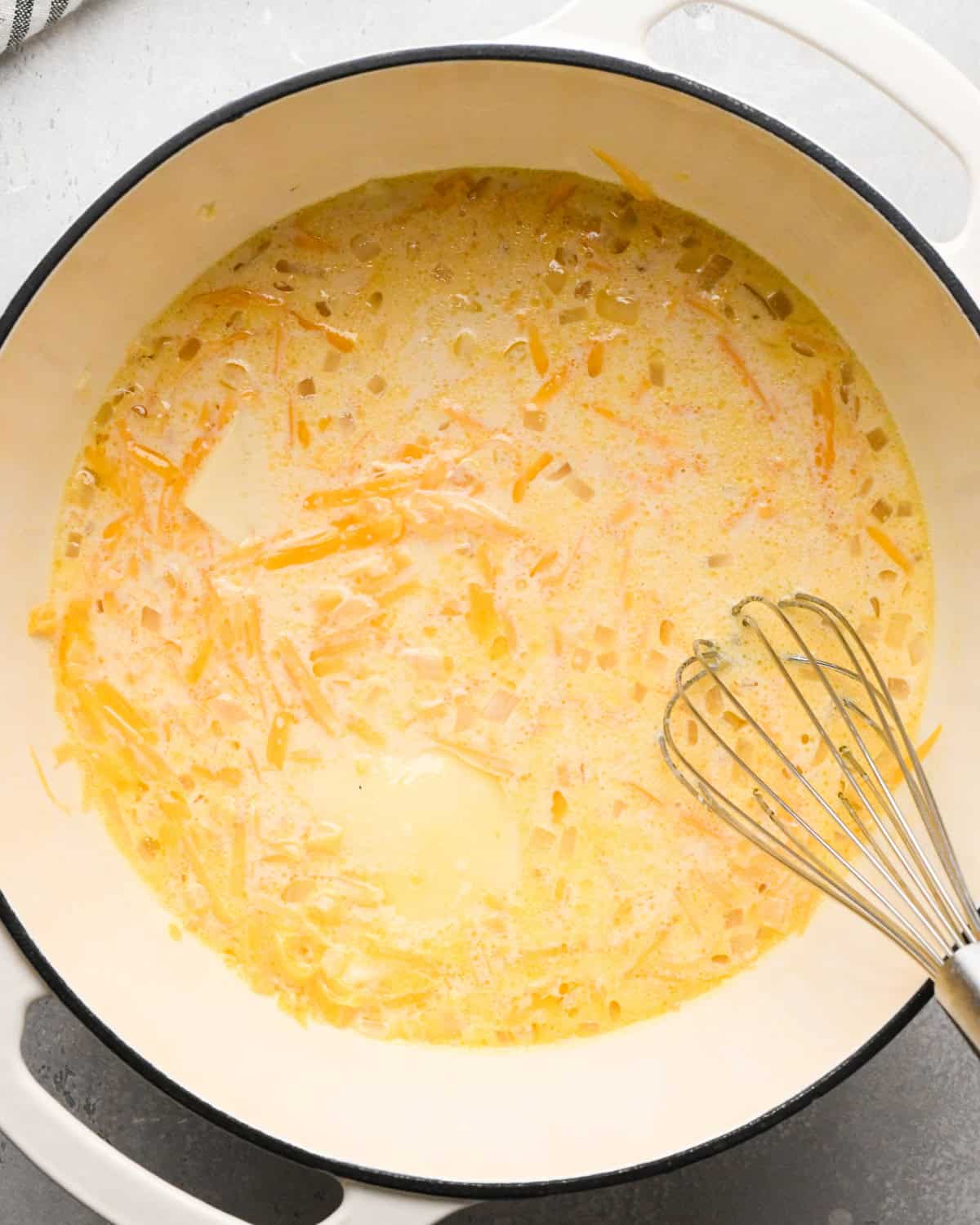 Making homemade queso: overhead photo of cheese being melted down in a large white pot. A metal whisk is stirring the sauce together as it simmers.