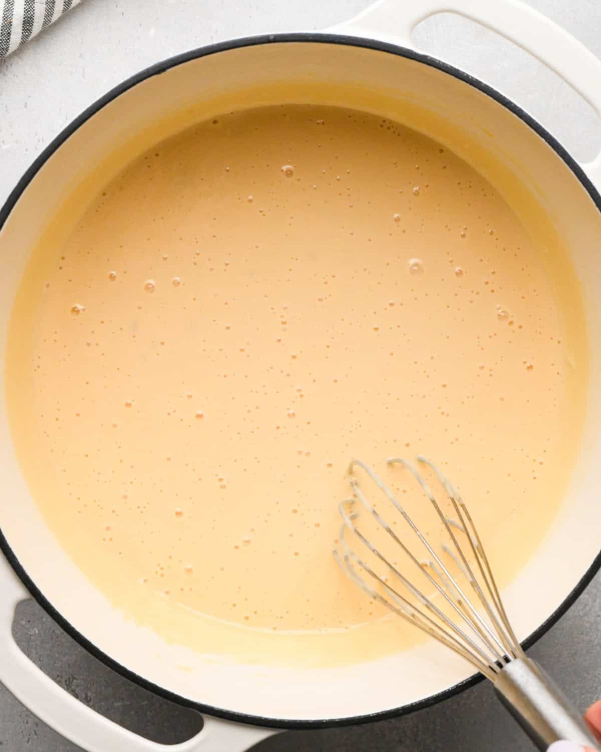 Making homemade queso: overhead photo of homemade queso simmering in a large white pot and being whisked together.