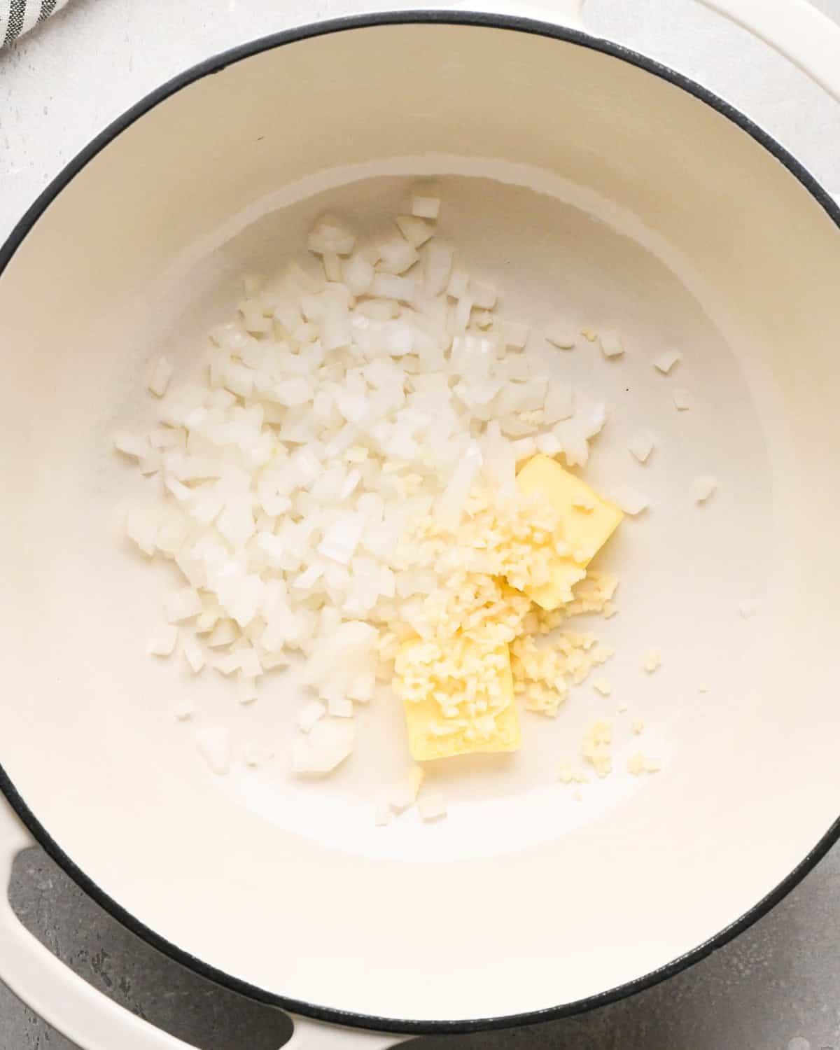 Making homemade queso: overhead photo of diced onion, minced garlic, and butter placed in a large white pot.