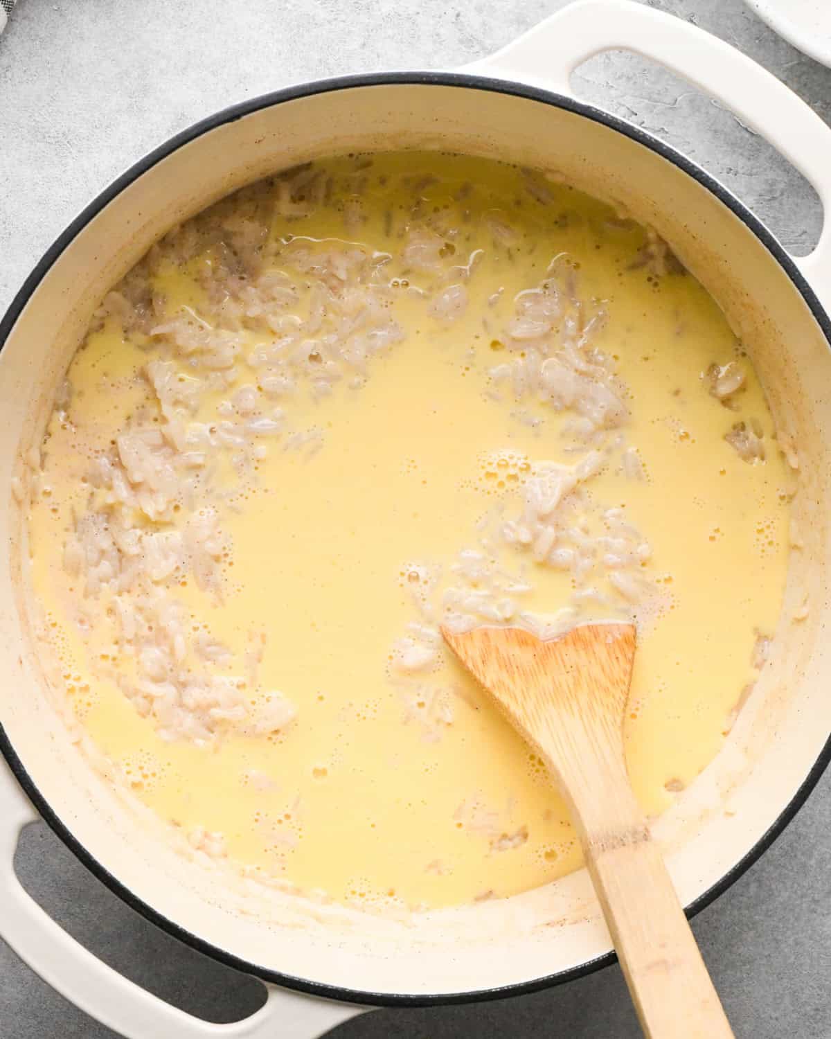 Making rice pudding: overhead photo of egg and milk mixture added to the large pot with the rice mixture. A wooden spoon is sitting in the pot.