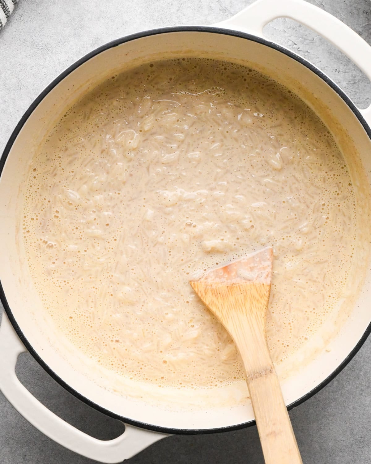 Making rice pudding: overhead photo of egg and milk mixture added to the large pot with the rice mixture and stirred together with a wooden spoon.