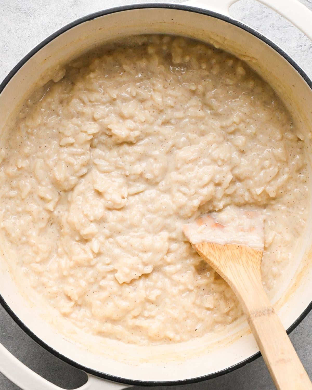 Making rice pudding: overhead photo of butter and vanilla added to a large pot with the rice pudding and being stirred with a wooden spoon.