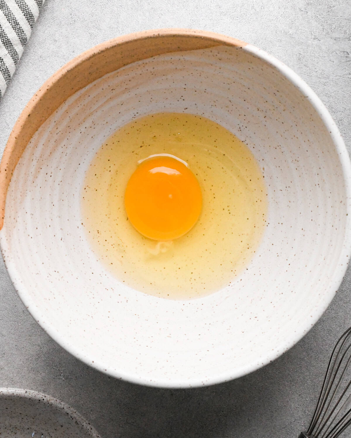 Making rice pudding: overhead photo of an egg cracked into a white speckled bowl.