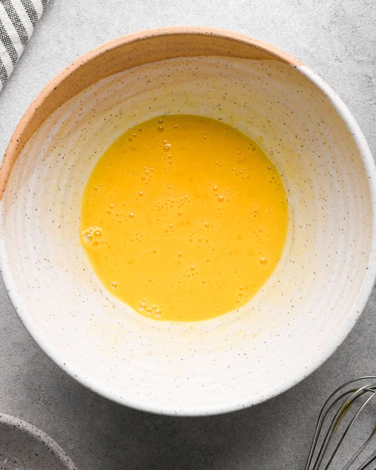Making rice pudding: overhead photo of an egg cracked into a white speckled bowl and beaten together.