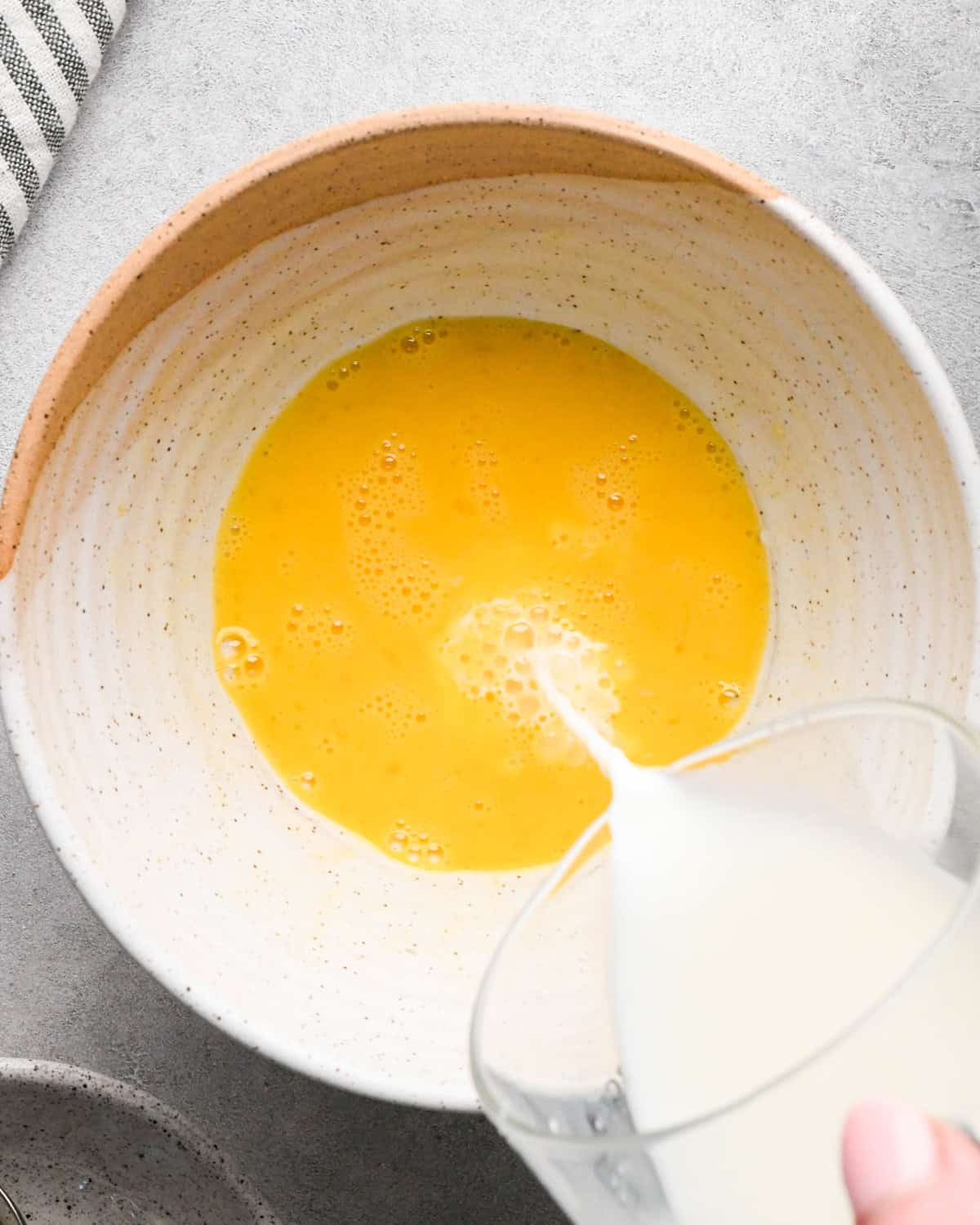 Making rice pudding: overhead photo of whole milk being poured into a bowl with a beaten egg.